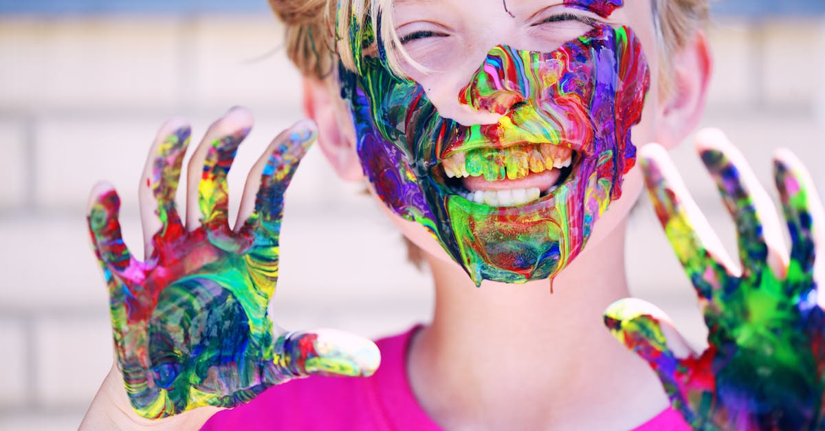 A joyful child with vibrant face paint and hands, expressing happiness and creativity.