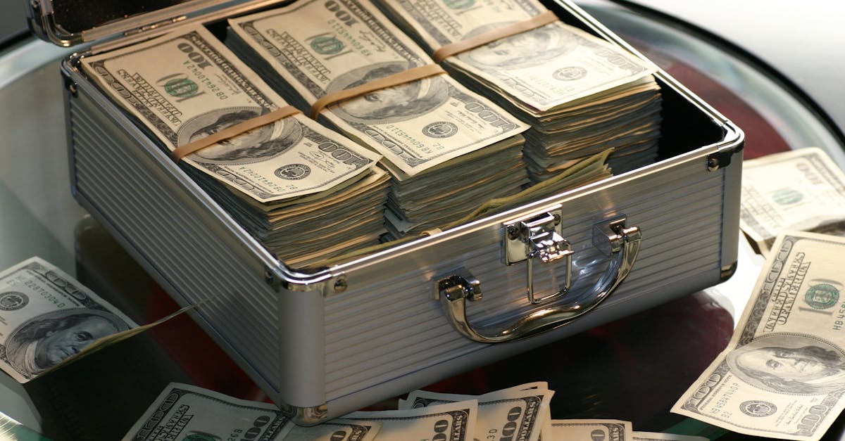 Open briefcase filled with stacks of hundred dollar bills on a glass table, representing wealth.