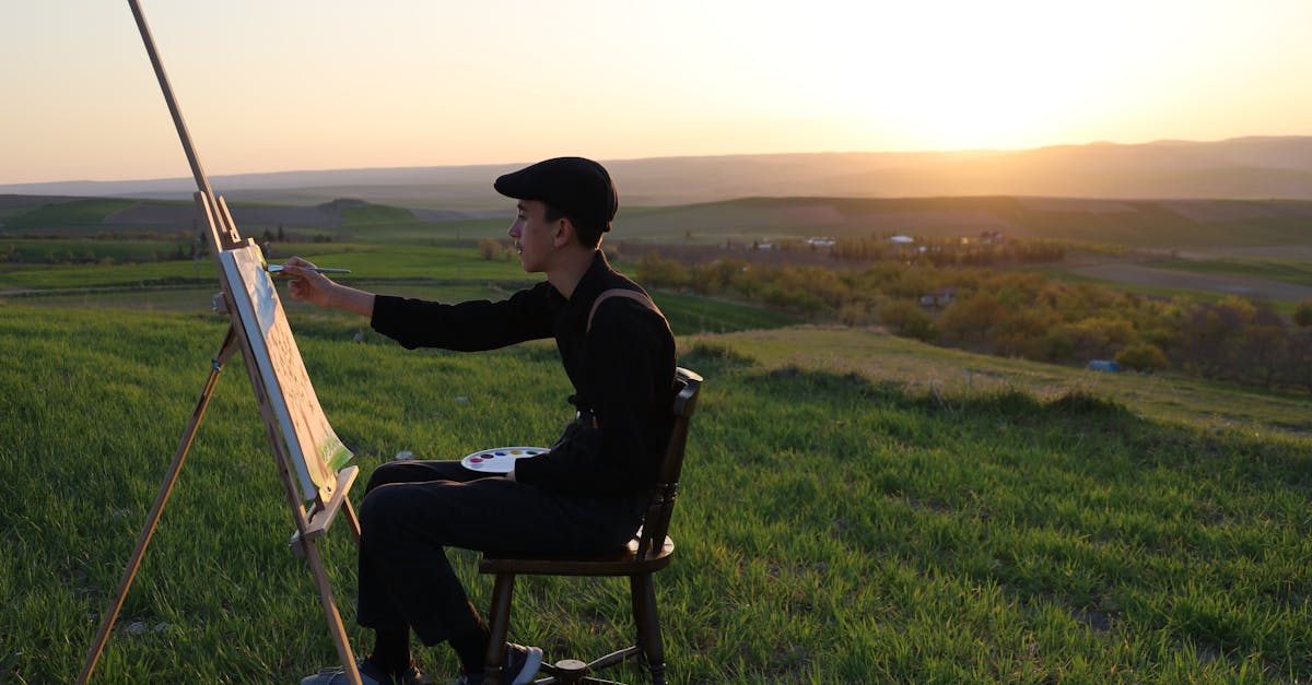 An artist immersed in painting outdoors on a hilltop during a calming sunset scene.
