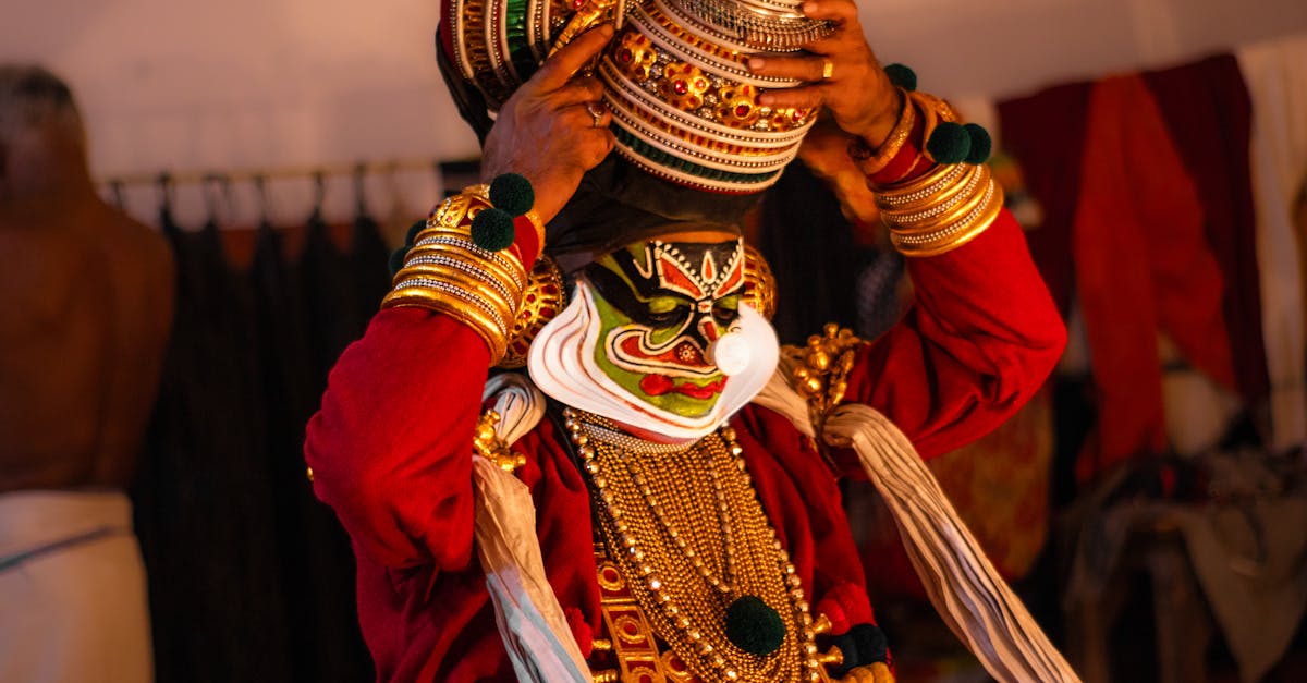A Kathakali artist wearing traditional attire and makeup, adjusting the headgear backstage.