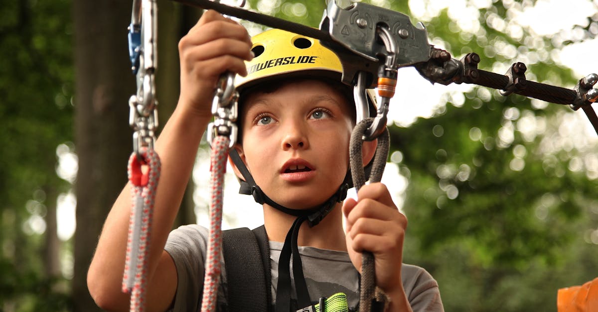 A young boy enjoying a rope climbing activity outdoors, wearing a helmet and using safety gear.