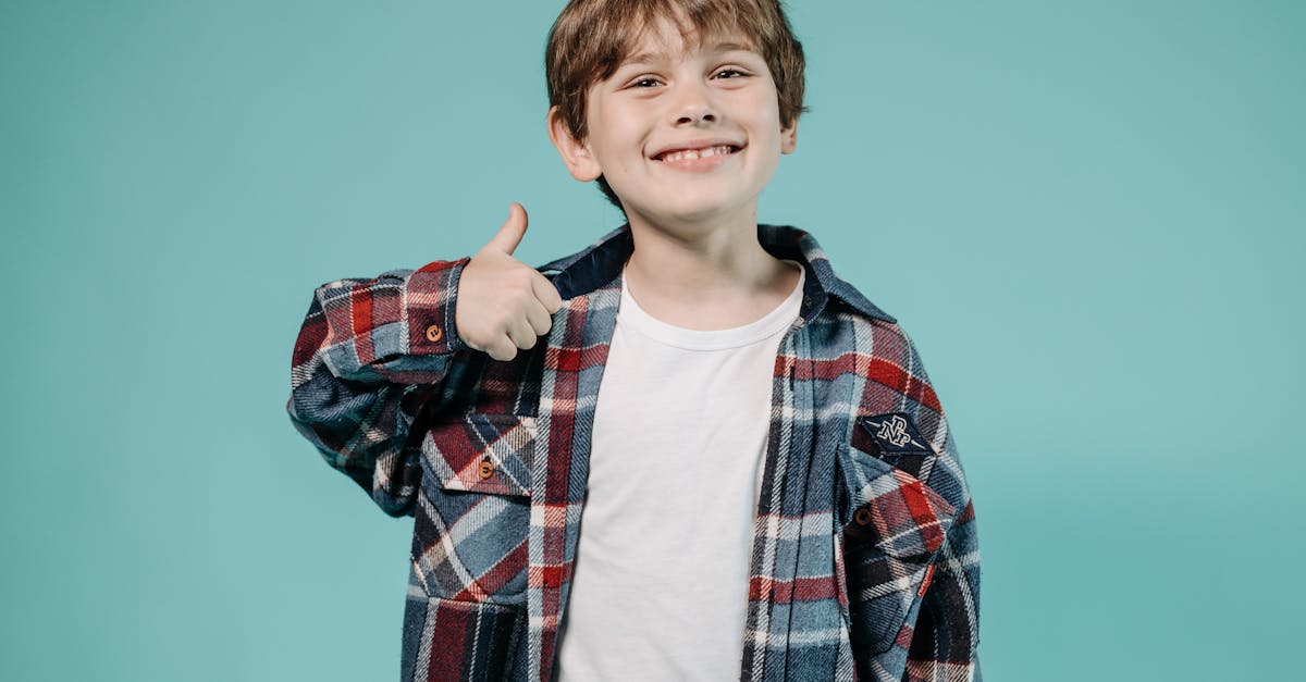 Smiling young boy in plaid shirt giving thumbs up with blue background in studio.