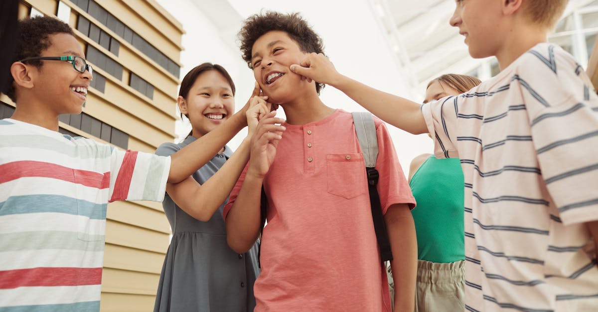 A group of cheerful schoolkids share a funny moment while pinching each other's cheeks.
