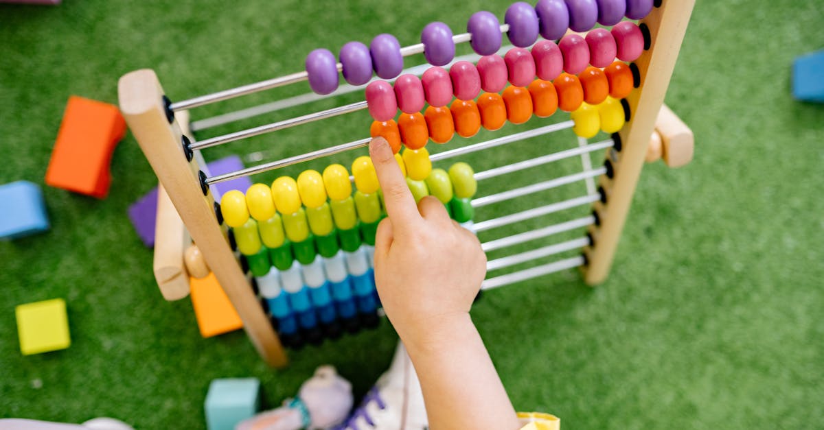 A child's hand using a colorful wooden abacus on green turf, emphasizing playful learning.