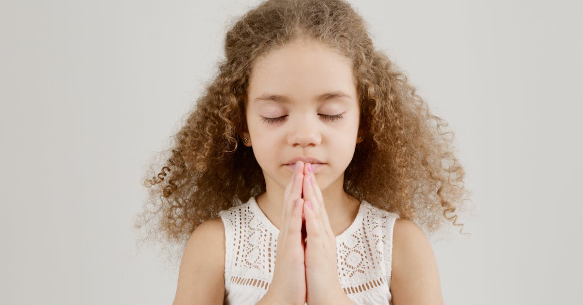 A young girl with curly hair and closed eyes is praying peacefully indoors.